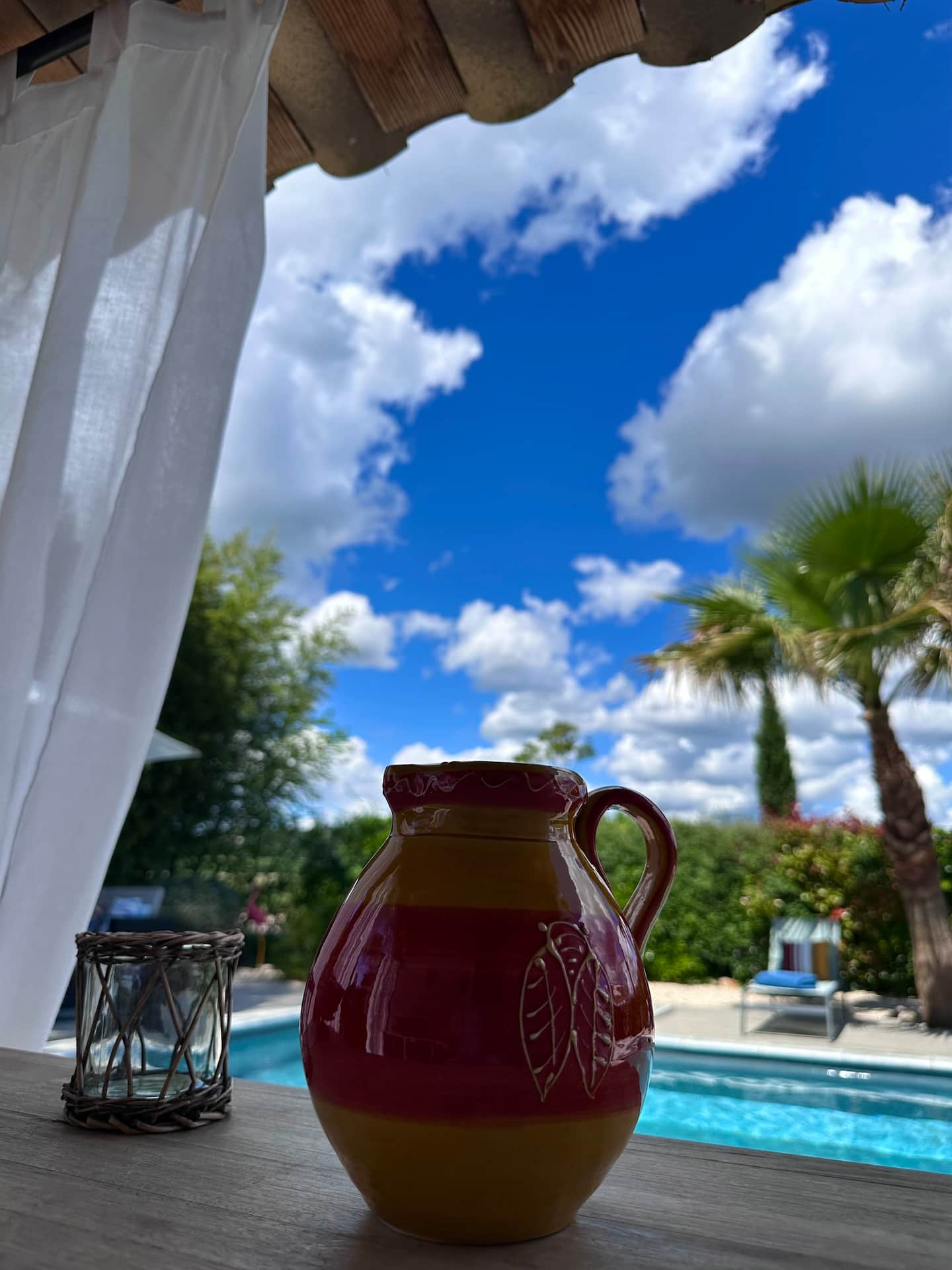 Ein provenzalischer Krug auf dem Tisch des Pool House, dahinter der Pool und die Palmen